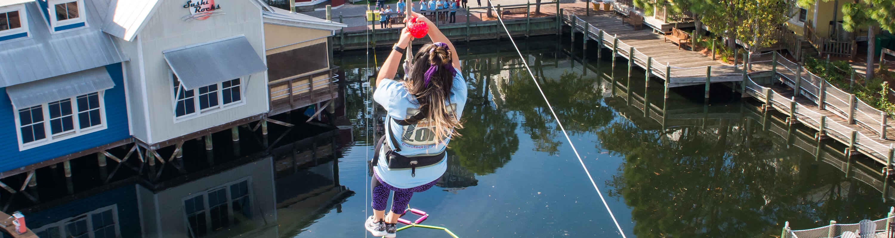 Rider ziplining across the lagoon at Baytowne Adventure Zone in the Village of Baytowne Wharf