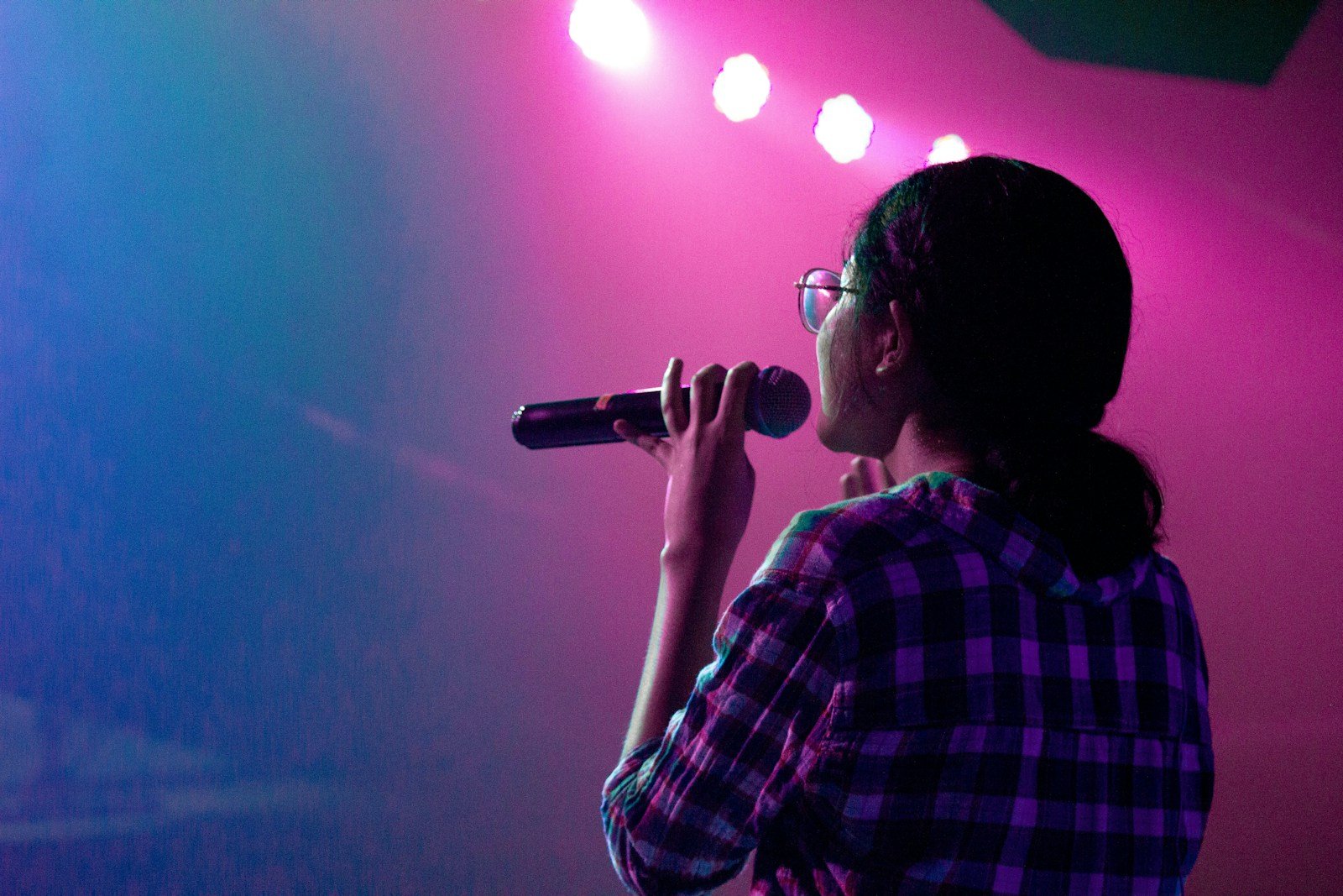 Woman singing into a microphone under stage lights