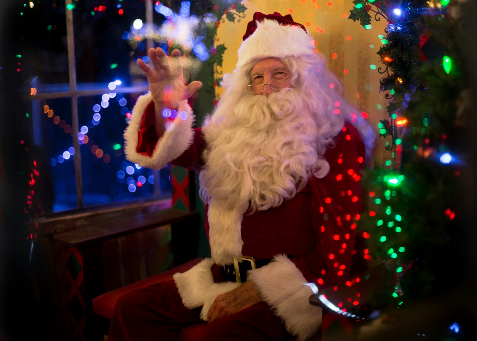 Santa Claus sitting beside a lit Christmas tree