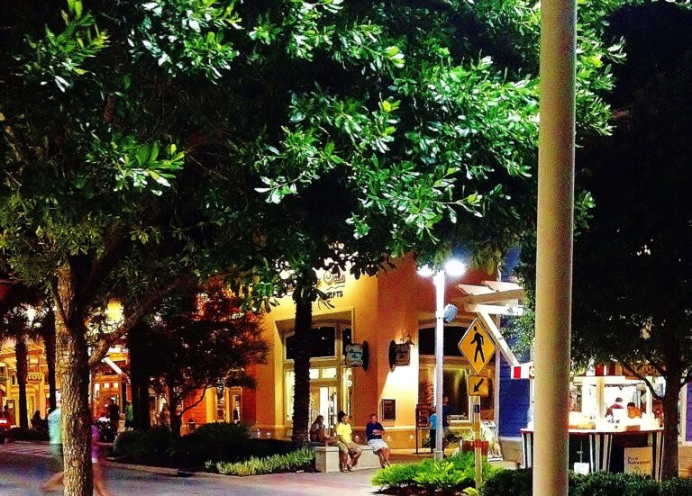 Tree-lined walkway and storefronts at Pier Park in Panama City Beach at night